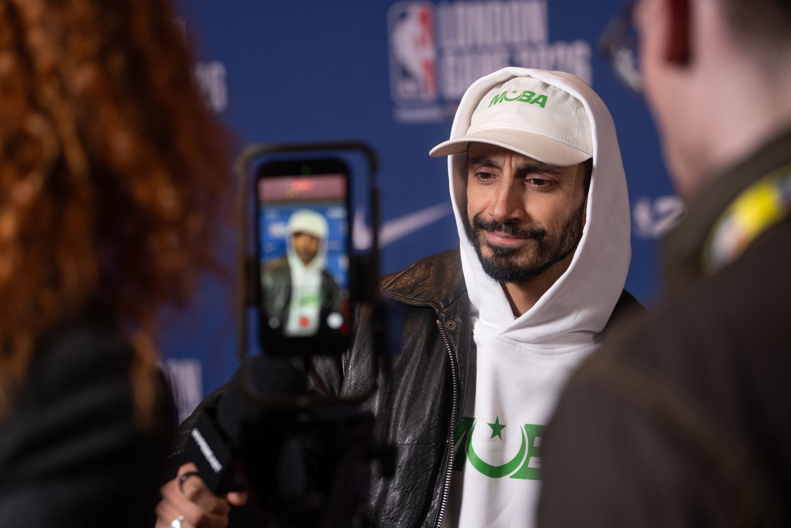 Image may contain Riz Ahmed Clothing Coat Jacket Adult Person Photography Crowd Hat Cap and Baseball Cap