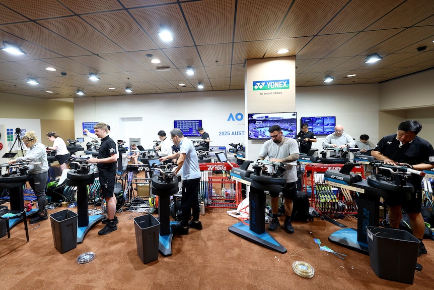 Multiple people work on racquet stringing machines.