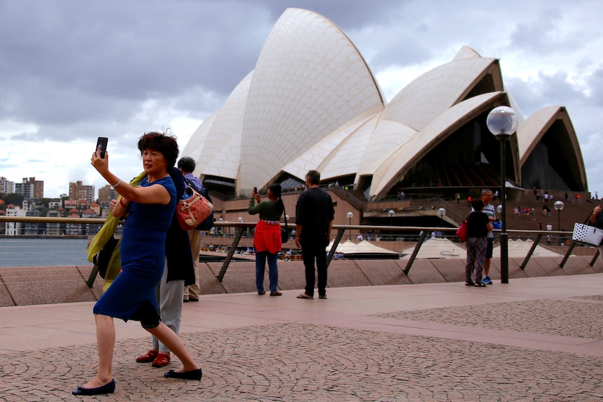 a Chinese tourist taking a self by using the Opera House as a background 