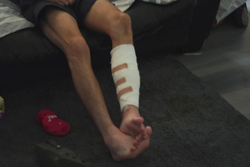 Kaleb Macqueen talks to media with his leg in a bandage after surviving a shooting