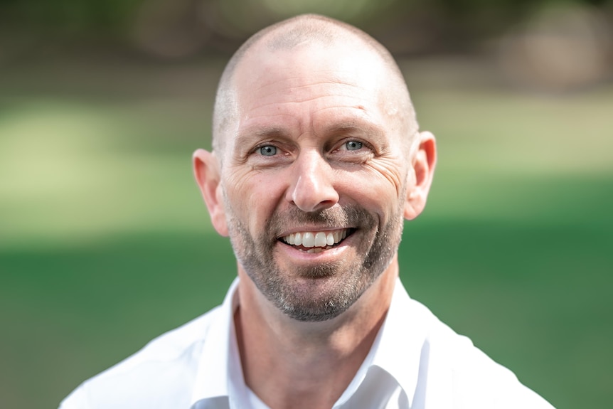 A man smiles at the camera with his arms crossed.