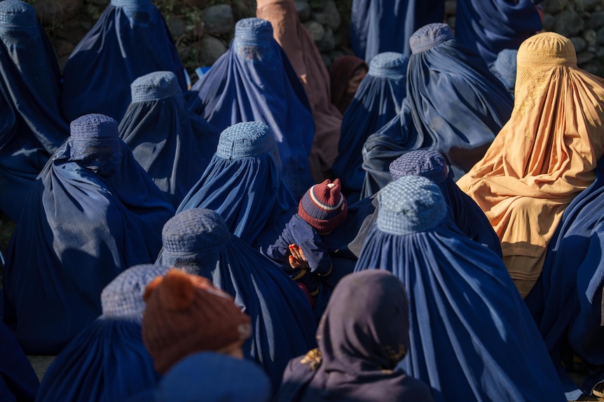 A group of women dressed in burqas and a baby sit on the ground in Afghanistan.