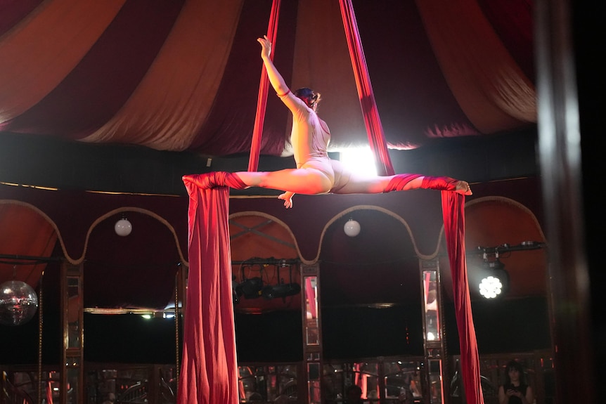 A performer uses silks to raise herself above the stage
