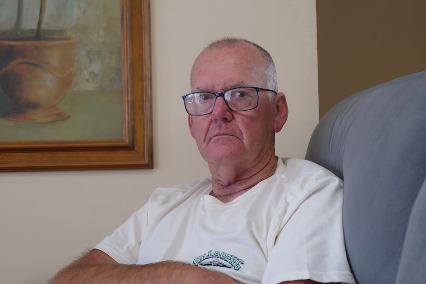 A man with glasses sitting on his couch with a disappointed expression. 
