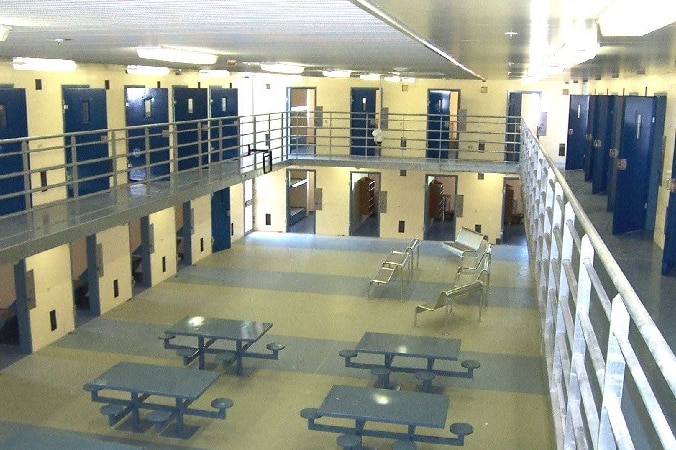 A common area inside a prison, featuring tables and chairs in an open space surrounded by cells.