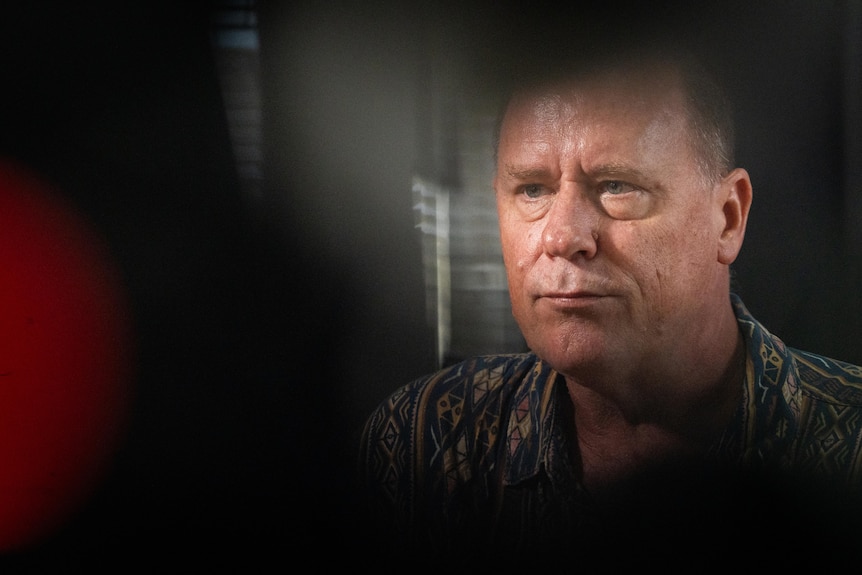 A man's face is framed by objects in the foreground