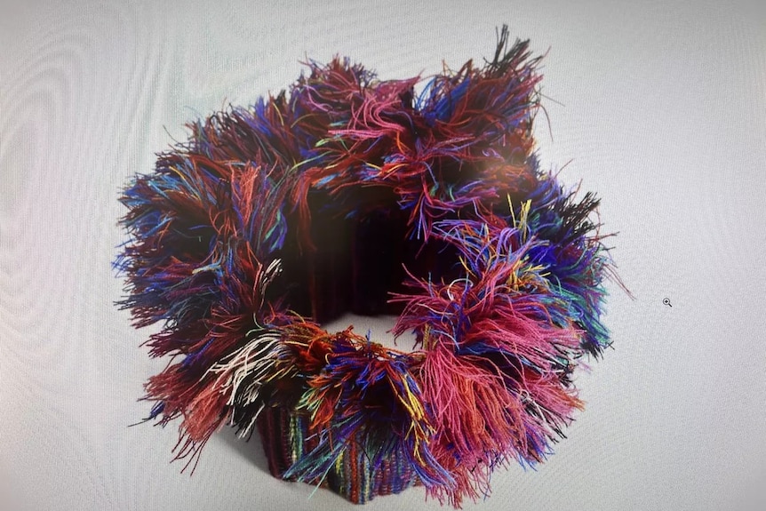 A ring-shaped textile artwork with lots of loose colourful thread ends poking up