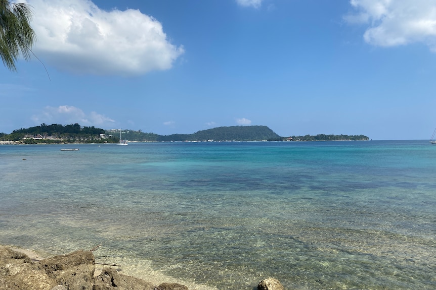 Turquoise waters in a bay with two islands and a headland in the background.