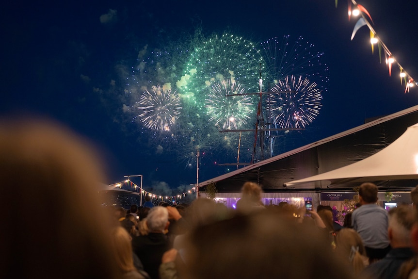 People gathering at a big colourful music and food festival with fireworks in the background.