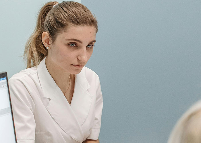 Young female doctor in white coat listening attentively to patient, highlighting unprofessional things doctors have said.