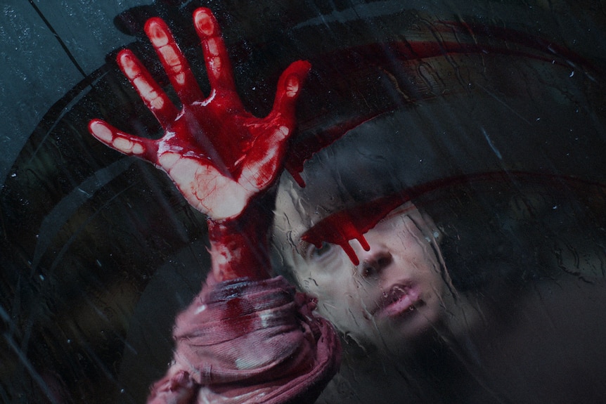 A woman smears blood in a circular motion on a window.