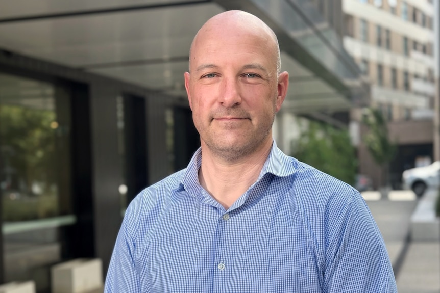 A man in a blue shirt smiles softly.