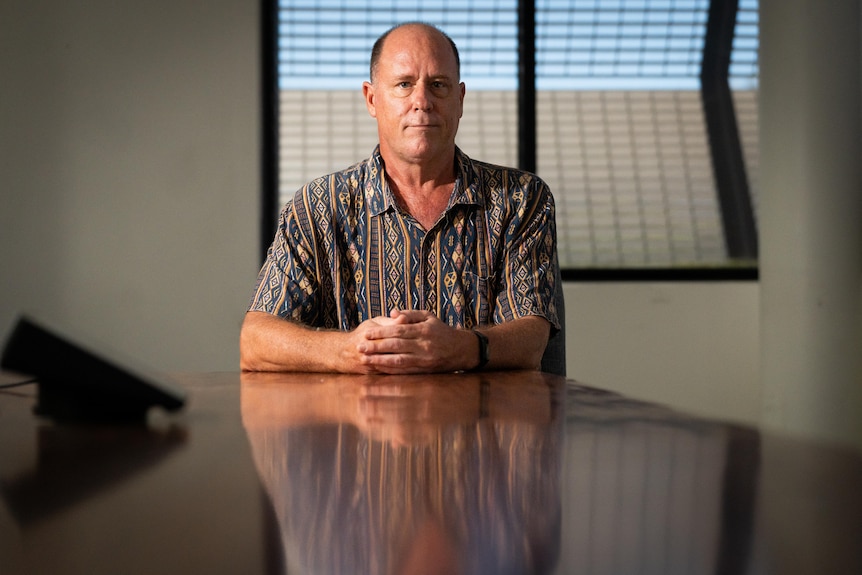 A man sits at the head of a long wooden table