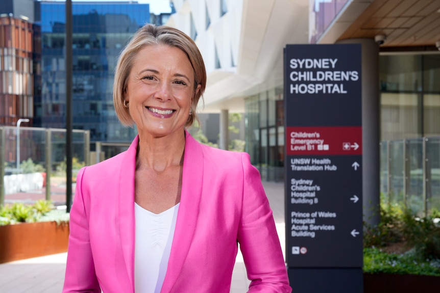 Kristina Keneally stands smiling wearing a pink blazer. 