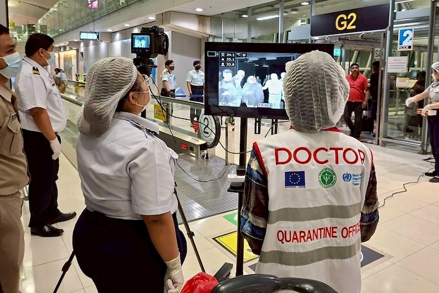 Medics wearing masks and hair nets wait to screen airline passengers.