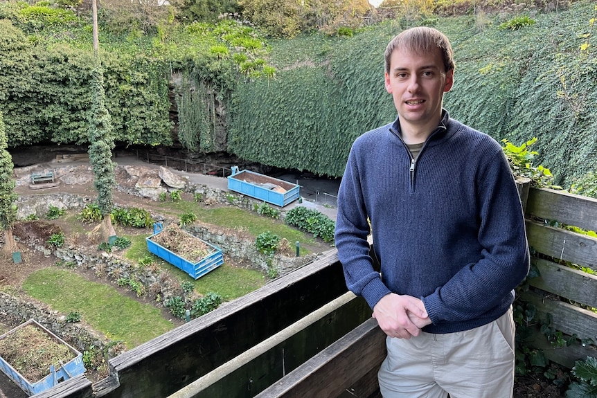 A man wearing a blue jumper standing in front of a large hole with plants inside