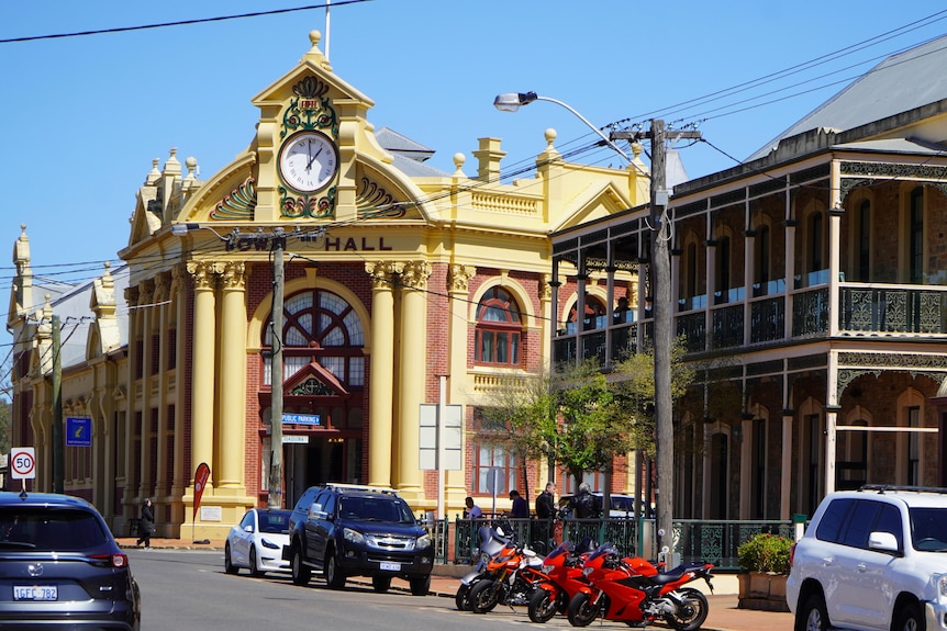 An elaborate brick building and terrace shops along a road.