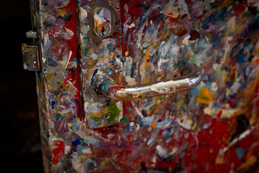 A door handle with various colours of paint on the handle and red door