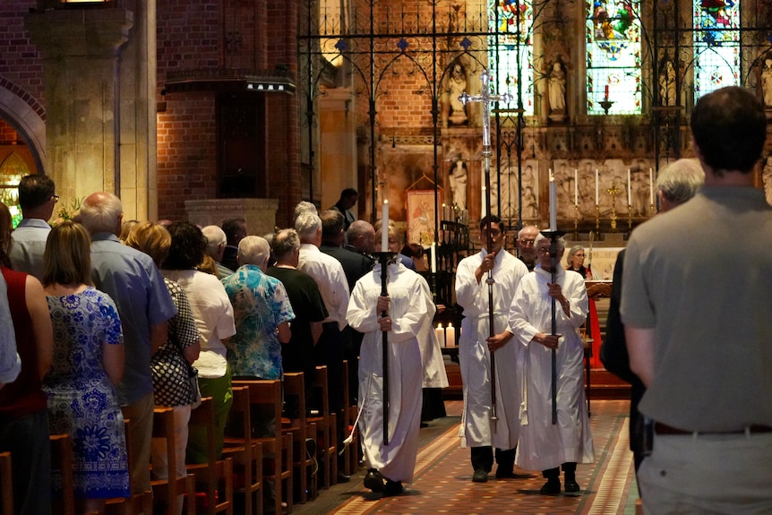 A group of people carry candles down a church aisle.