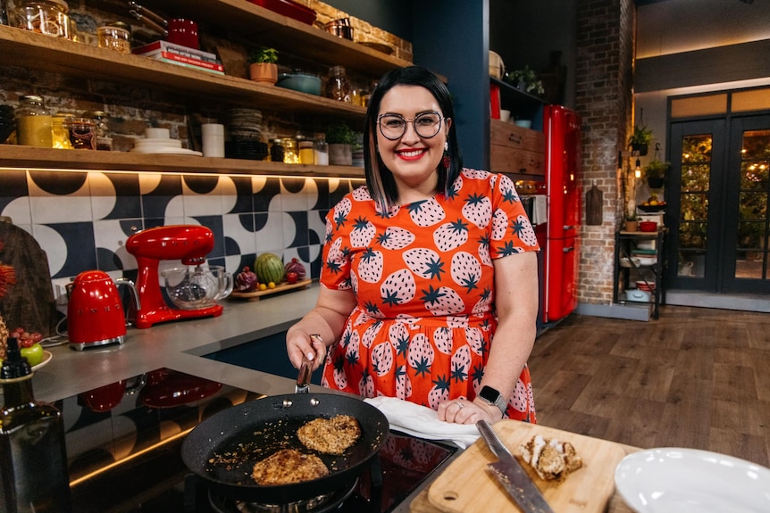 A woman with shoulder-length brown hair and blond streaks standing over a frying pan in a kitchen.