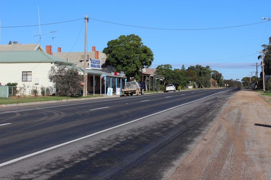 A country town road passing a small shop and a couple of parked cars.