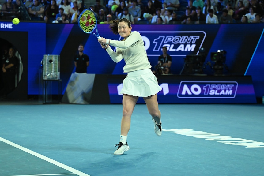 A woman plays a double-handed backhand while playing tennis on a blue court with people sitting in the stands behind her