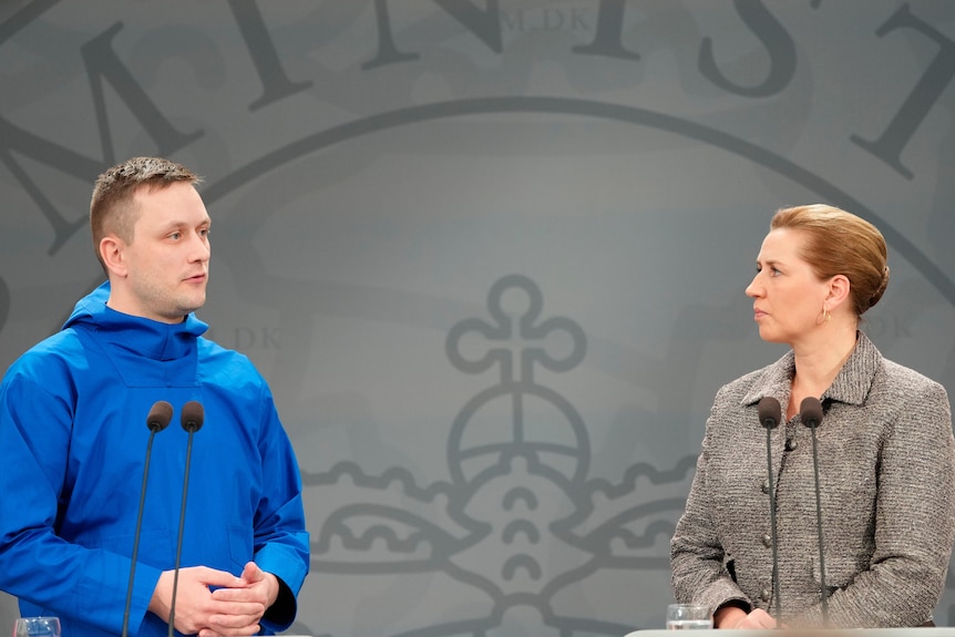 Jens-Frederik Nielsen and Mette Frederiksen sit apart at a desk, talking.