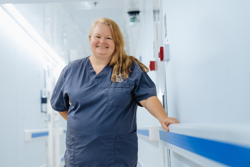 a woman in scrubs poses in a hospital corridor