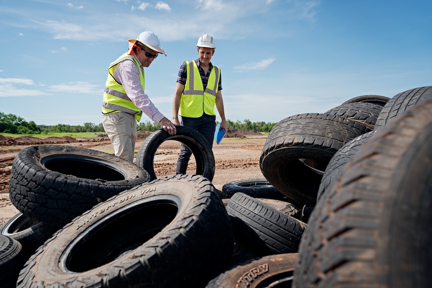 Two men in high-vis vests inspecting a pile of discarded tyres.
