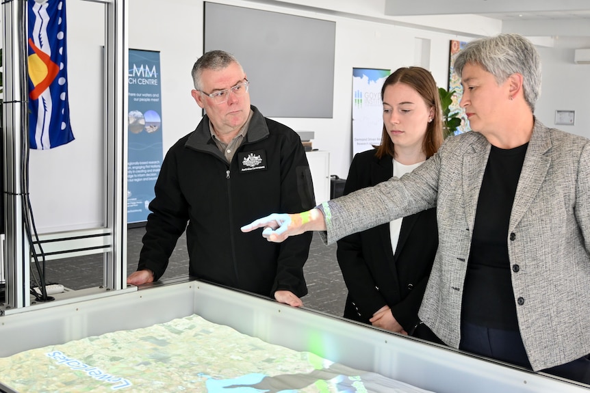 Murray Watt stands in front of Penny Wong at a water front