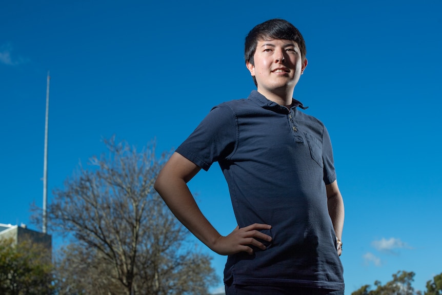a man in his twenties with a bowl cut, wearing navy polo, blue sky backdrop.