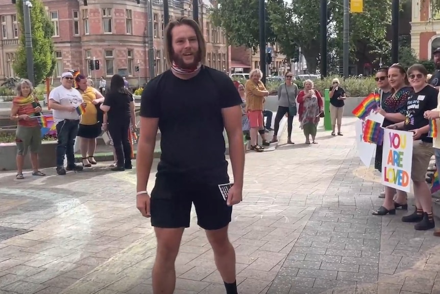 A man dressed in black speaks to people gathered outside a public building.