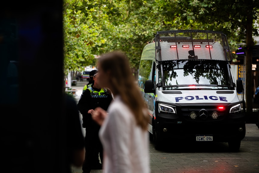 A police van driving down a pedestrian mall with people walking in the foreground.