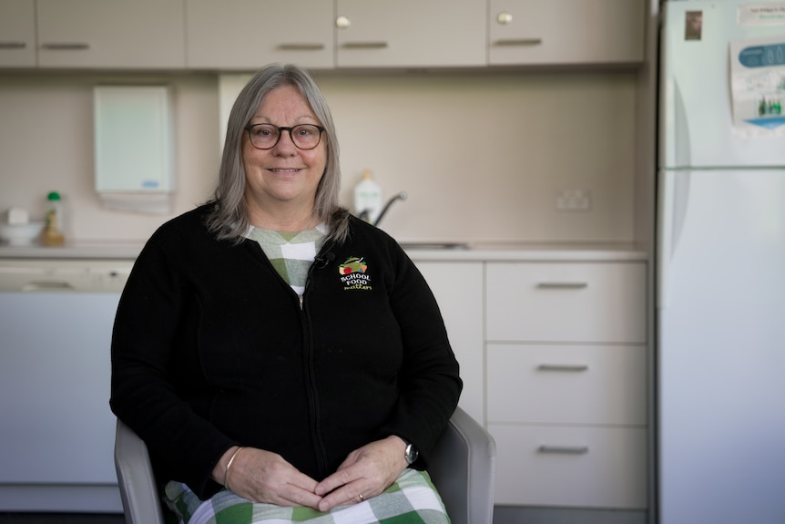 Woman sitting on a chair in front of a kitchen, smiling for photo