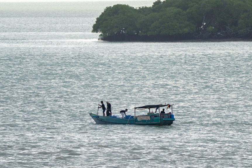 A small wooden boat with several occupants. It floats on the ocean near a headland.