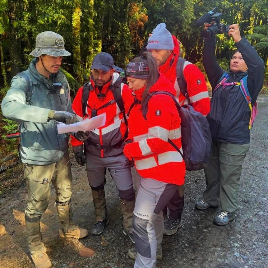 A group of five people in high-vis gear look and point at a map.