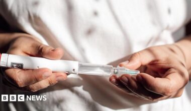 A close up of a health professional, in white clothing. They're holding a weight loss drug - in the form of a tube or syringe - that is ready to be injected.