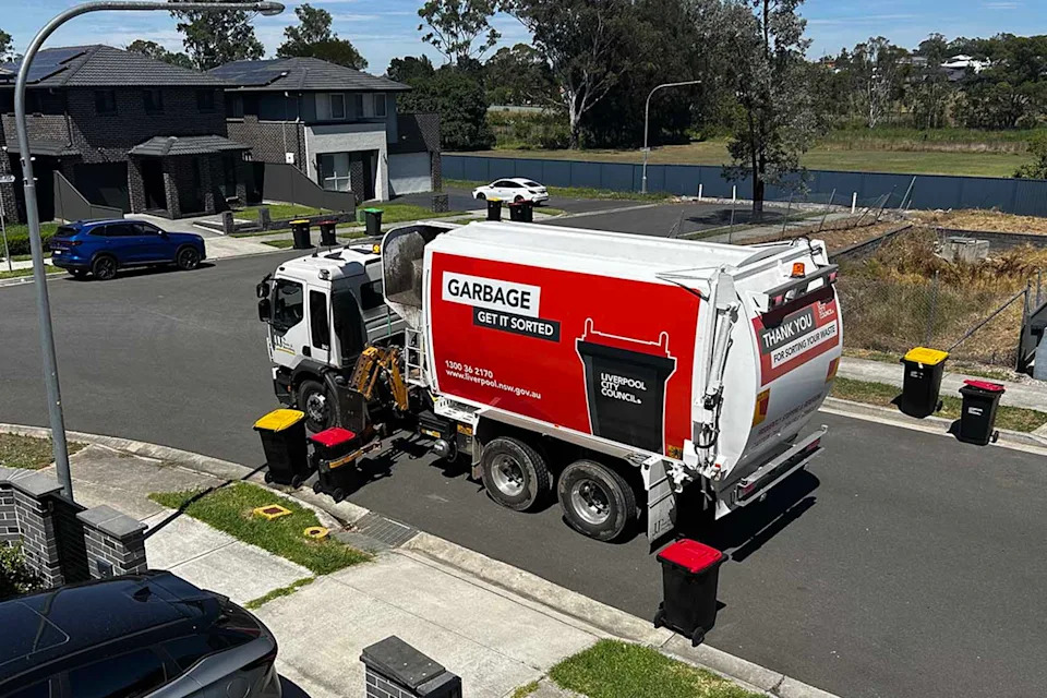 A garbage truck picks up a red bin from a suburban Sydney street