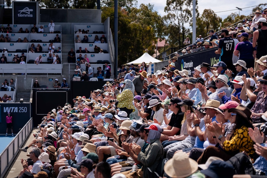 People sitting in sports stand watching a tennis match