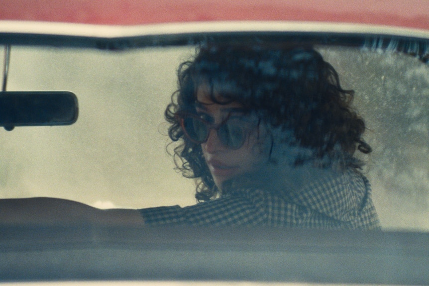 A woman in sunglasses looks through the back window of a car