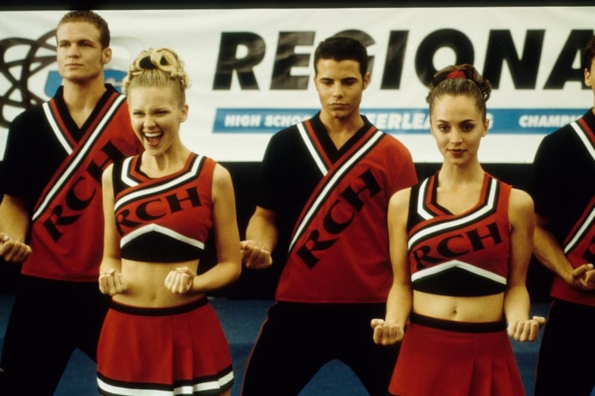Teen girls in red cheerleading uniforms stand in front of teen boys in red uniforms