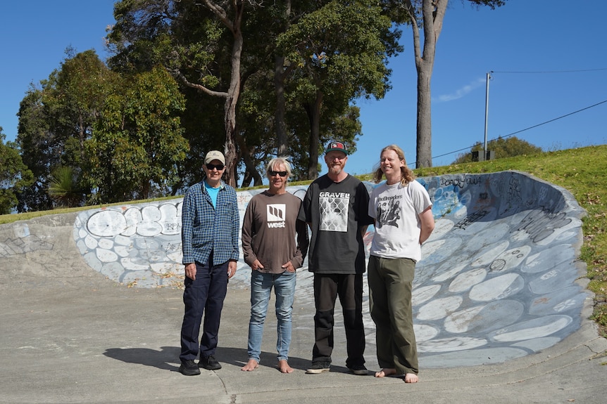 The four men stand together at a skate park. 