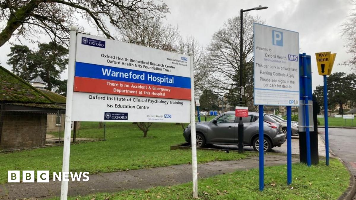 A sign outside a hospital saying Warneford Hospital. There's a carpark in the background and some autumnal trees.