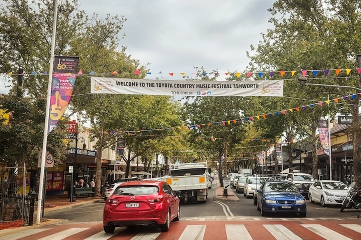A road in a main busy street with a banner above saying welcome to the toyota country music festival tamworth.
