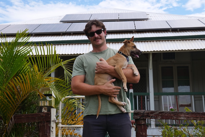 man smiling and holding dog in front of home