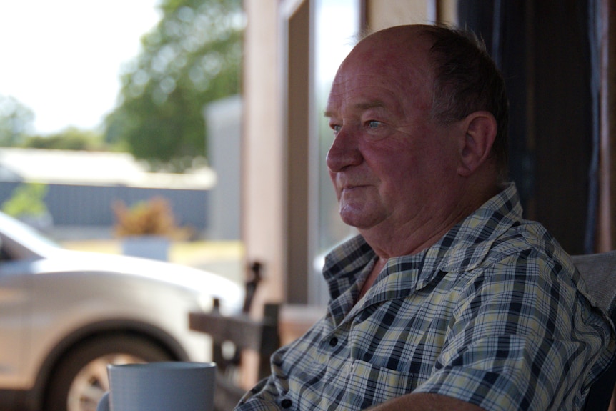 A man in a checked shirt looks to the side.