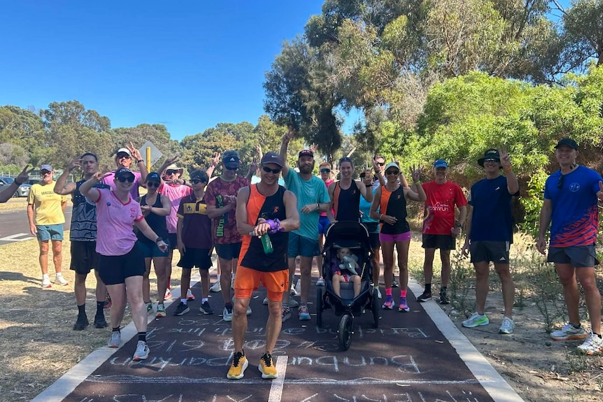 A wide shot of about 20 people standing around on a running track