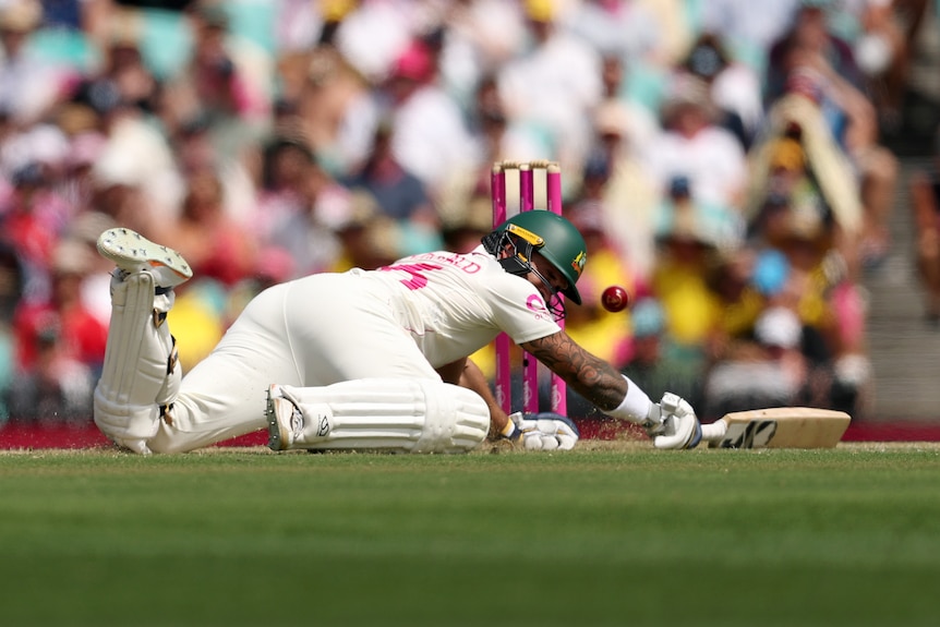 A cricket batter in whites dives into his crease with ball flying towards stumps