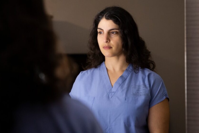 A photo of Arghavan Salles wearing light blue scrubs, standing in a dark room