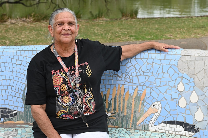 Aunty Jemmes Handy is pictured wearing a black t-shirt and is seated outdoors looking at the camera. 